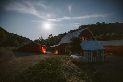 sun setting behind a hill with a barn in the foreground