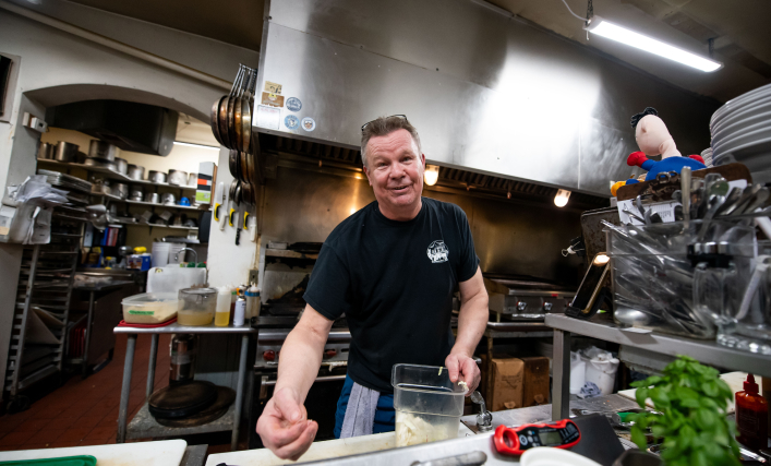 A chef in a kitchen looking directly at the camera while prepping food.