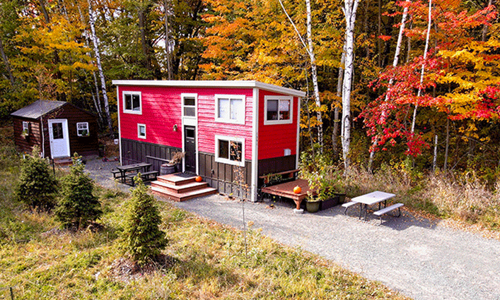 A red tiny house tucked near vibrant autumn trees. A red tiny house tucked near vibrant autumn trees.